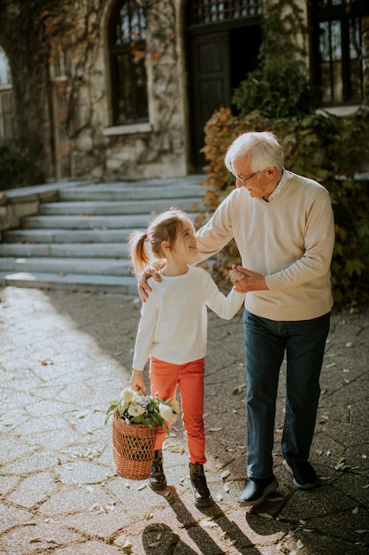 Grandfather having fun with his cute little granddaughter who holding basket full of flowers