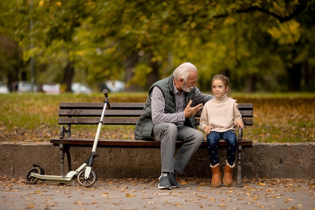 Grandfather spending time with his granddaughter on bench in park on autumn day