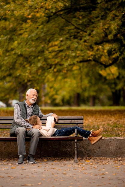 Grandfather spending time with his granddaughter on bench in park on autumn day