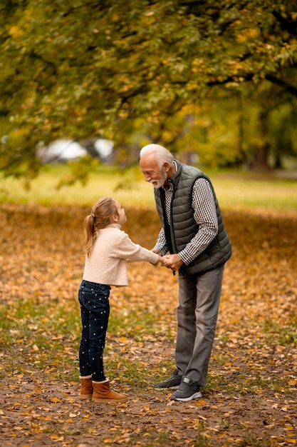 Grandfather spending time with his granddaughter in park on autumn day