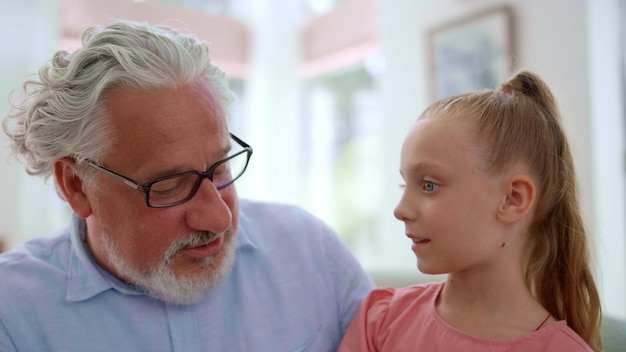 Grandfather talking with granddaughter at home Girl sitting on grandfather laps