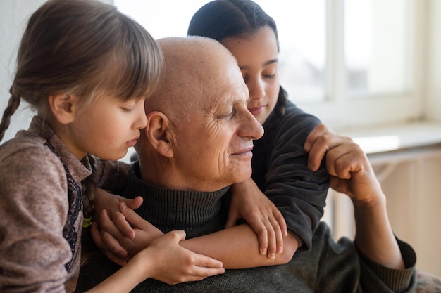 grandfather and two granddaughters hugging on sofa at home.