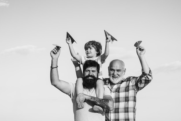 Grandfather with son and grandson having fun in park happy child playing with toy paper airplane aga