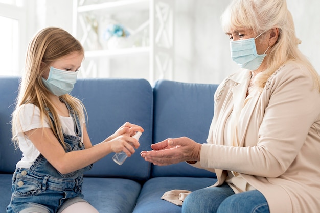 Grandma and girl with mask using sanitizer