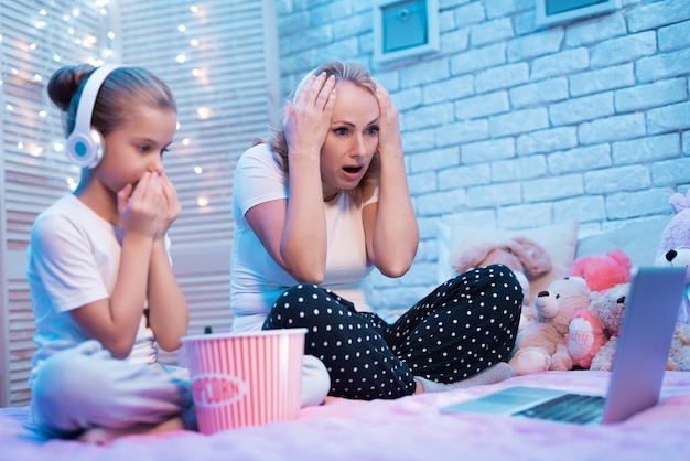 Grandmother and granddaughter are shoked watching movie at night at home.