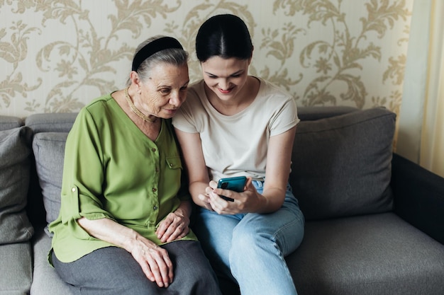 Grandmother and granddaughter look at the smartphone while sitting on the couch Looking at photos on the phone