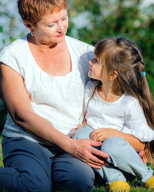 Grandmother and granddaughter sitting on the lawn on a summer day The little girl listens attentively to her grandmother