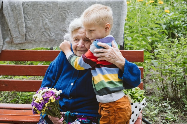 Photo grandmother and grandson embracing while sitting at park