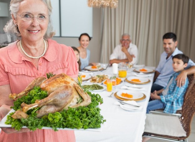 Grandmother holding chicken roast with family at dining table