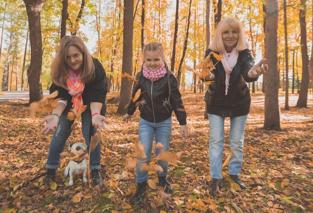 Grandmother and mother with granddaughter throw up fall leaves in autumn park and having fun generat