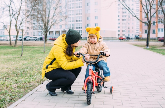 Grandmother teaches small child to ride bike for the first time in city spring