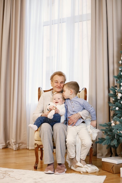 Grandmother with her granddaughter and grandson sitting near Christmas tree