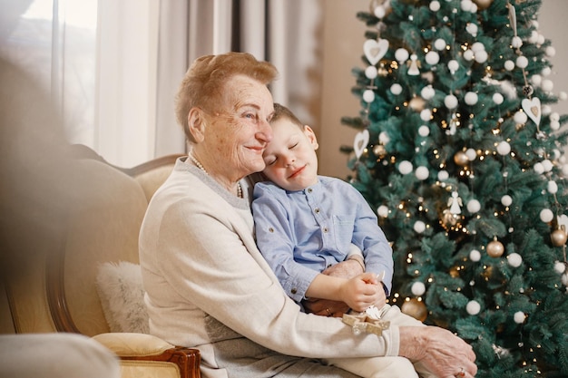 Grandmother with her grandson sitting near Christmas tree on a chair