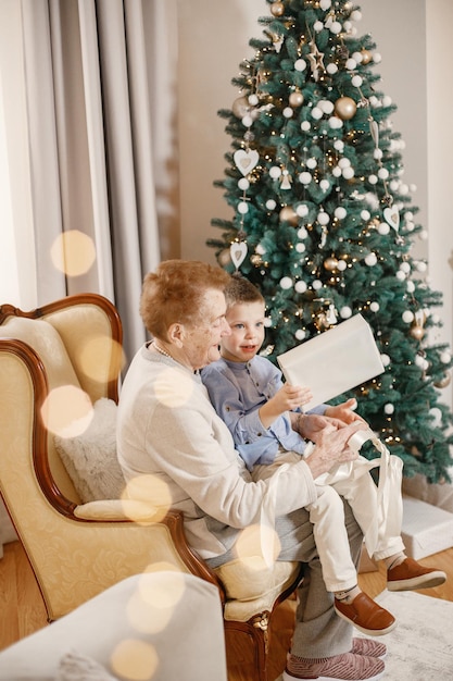 Grandmother with her grandson sitting near Christmas tree on a chair