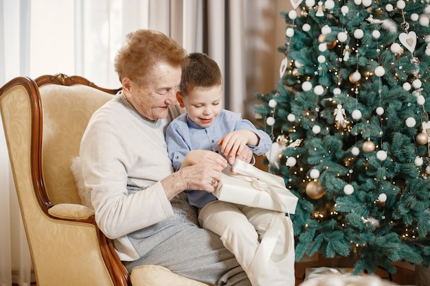 Grandmother with her grandson sitting near Christmas tree on a chair