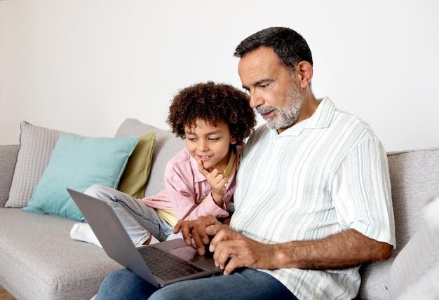 Grandpa and little grandson using laptop for online entertainment indoors