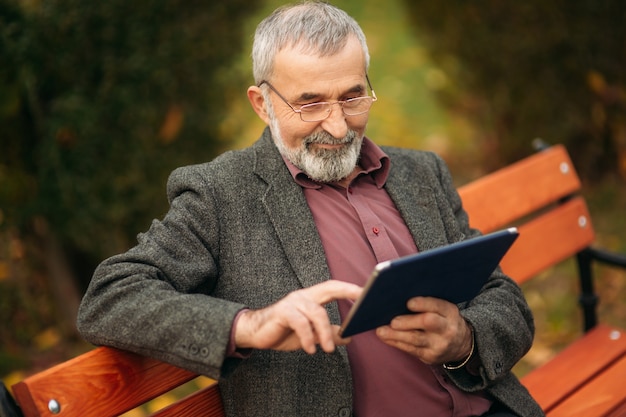 Grandpa use a tablet sitting in the pakr on the bench