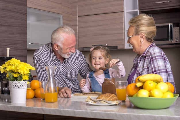 Grandparents and granddaughter preparing pancakes with chocolate cream in the kitchen