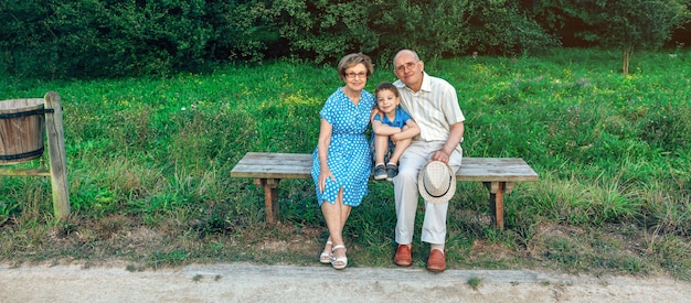 Grandparents and grandson posing for a photo sitting on a bench outdoors