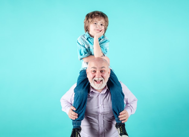 Grandson child and grandfather piggyback with funny face isolated on blue in studio granddad and cut