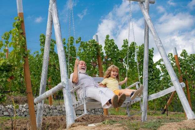 Grandson child and grandfather swinging in summer garden granddad and grandchild sitting on swing in