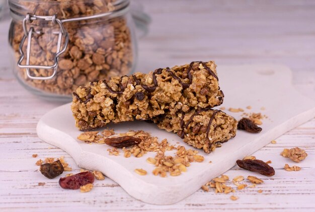 Granola bars with nuts and raisins and pieces of chocolate on a white wooden board