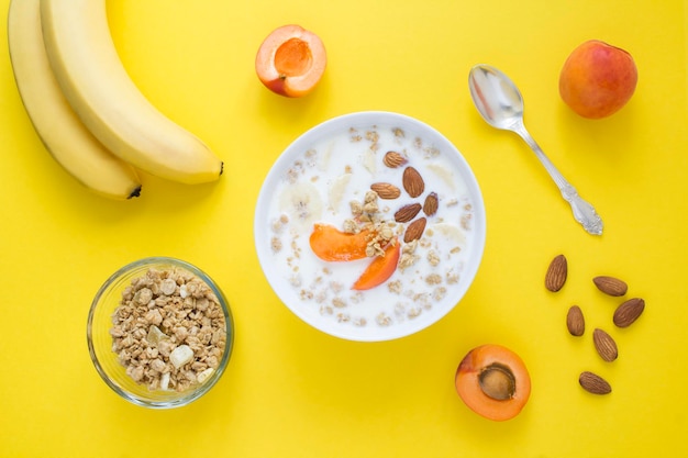 Granola breakfast with milk fruits and almonds in the white bowl on the yellow background Top view Closeup