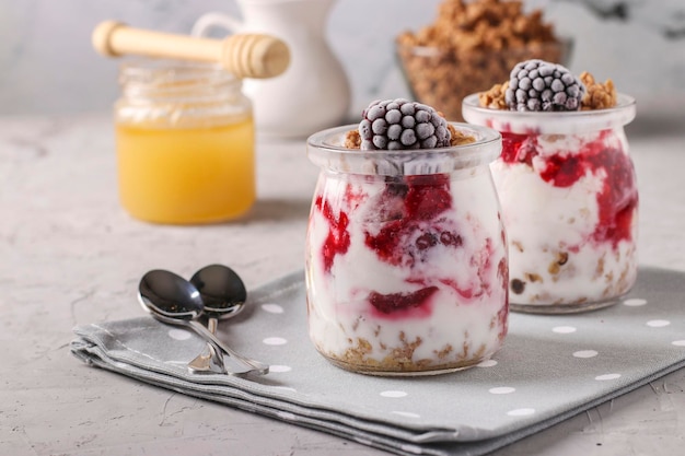 Granola crispy honey muesli with frozen blackberries, cottage cheese and natural yogurt, a delicious and healthy breakfast, located in glass jars on a gray background, Closeup