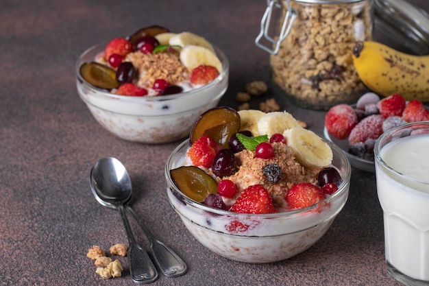 Granola crispy muesli with natural yogurt frozen berries and fruit and nuts in two glass bowls on brown background