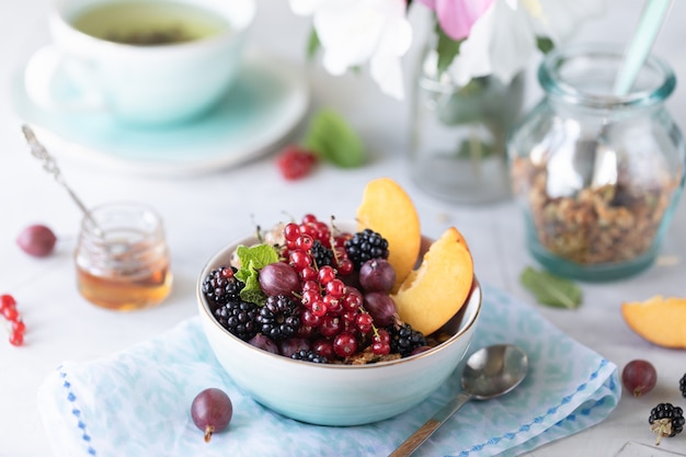 Granola or muesli with berries and fruits for a healthy breakfast in the morning with a bouquet of summer flowers on a light table.