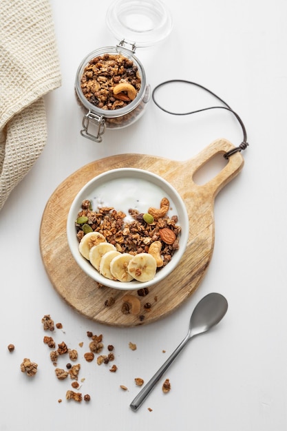 Photo granola with banana and nuts on a wooden board on a white table with a napkin and spoon