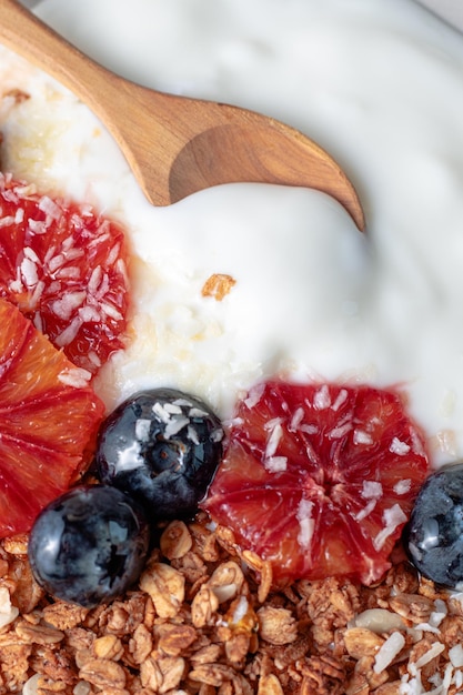 Granola with greek yogurt decorated with blood oranges blueberry and coconut and wooden spoon close up