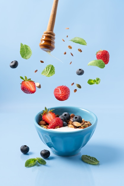 granola with yogurt and berries in bowl on blue background