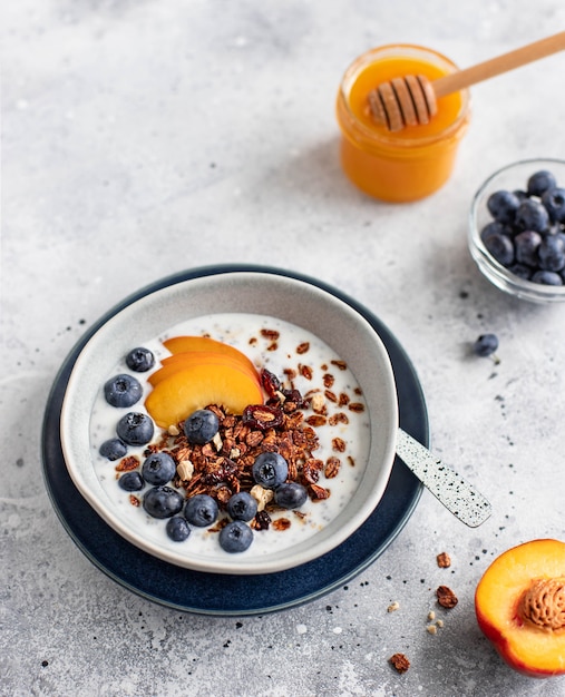 Granola with yogurt, blueberries, peach and honey on a light background