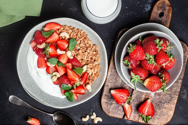 Granola with yogurt and strawberries in a plate on a dark background