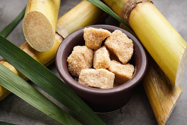 Granulated brown sugar sugarcane and green leaf on a gray background closeup