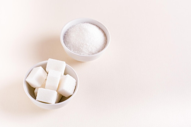 Granulated sugar and sugar cubes in bowls on a pink background Choosing between types of sugar