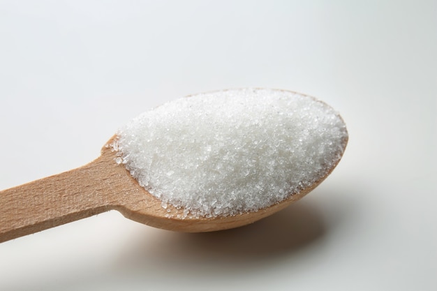 Granulated sugar in wooden spoon on white background