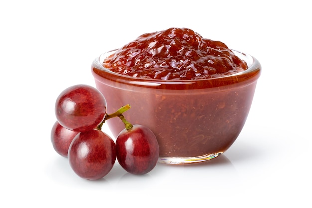 Grape jam in glass jar with red grapes isolated on white background