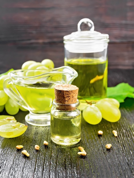 Grape oil in a bottle, gravy boat and jar, berries of green grapes on the background of dark wooden board