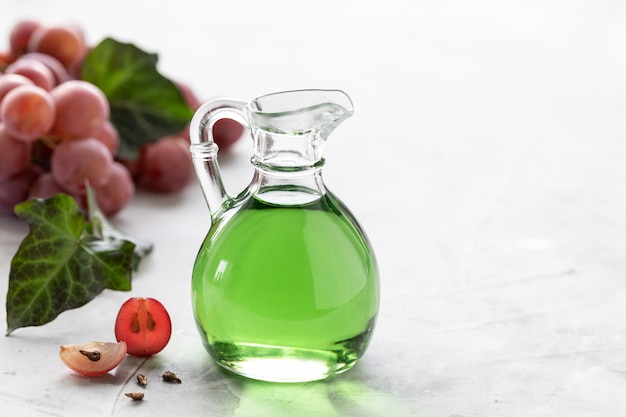 Grape seed oil in a glass bottle with a bunch of grapes.