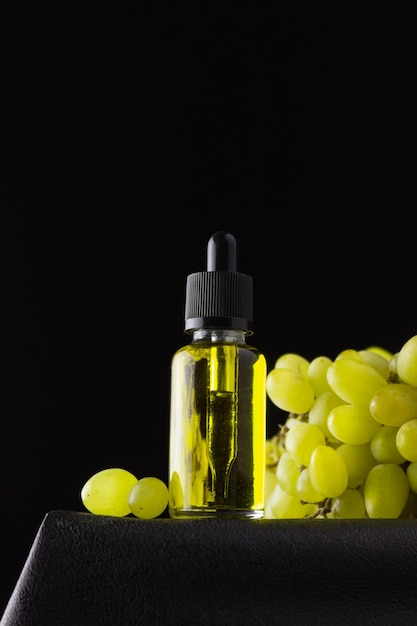 Grape seed oil in a glass bottle with a pipette and green grapes on a black background. Organic bio cosmetics with plant ingredients.