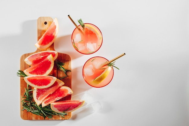 Grapefruit and Cucumber Gin Cocktail on glasses and a wooden cutting board on white background