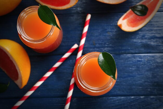 Grapefruit juice in bottles and fresh fruits on dark blue wooden background