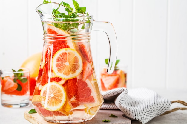 Grapefruit lemonade with lemon and mint in glass jug.