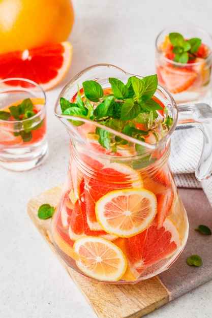 Grapefruit lemonade with lemon and mint in glass jug.