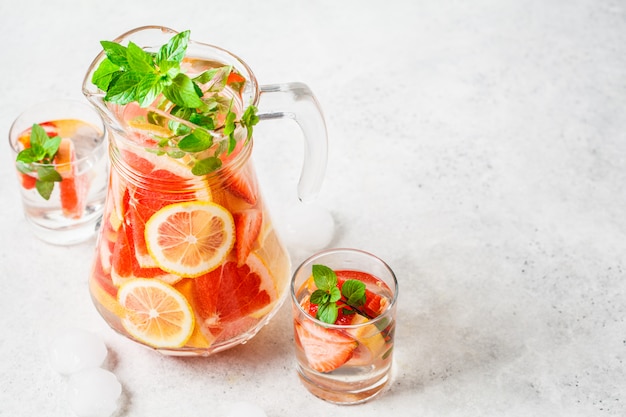 Grapefruit lemonade with lemon and mint in glass jug.