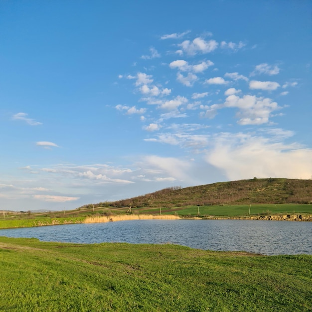 A grassy hill with a small pond in the foreground and a hill in the background.