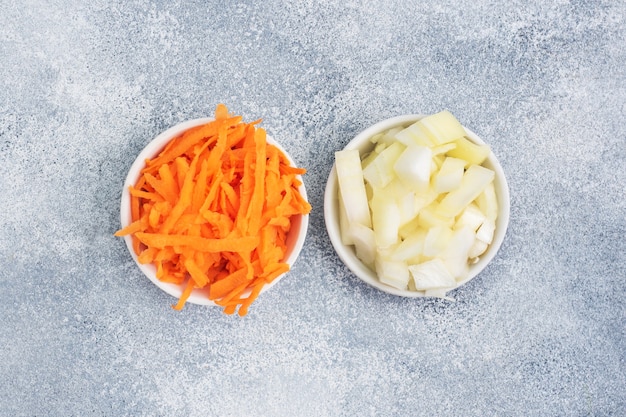 Grated carrots and chopped onions in a white plate. Raw vegetables, ingredients for roasting. gray table, copy space, top view.