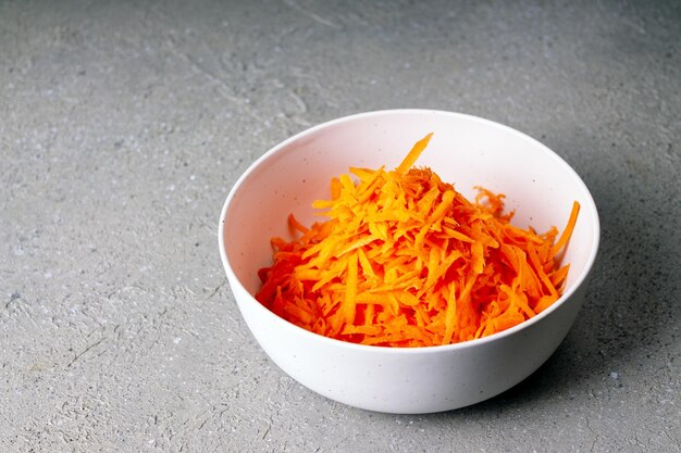 Grated carrots in a white ceramic plate on a gray background, copy space